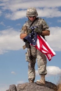 US Soldier staning on a rock holding American Flag